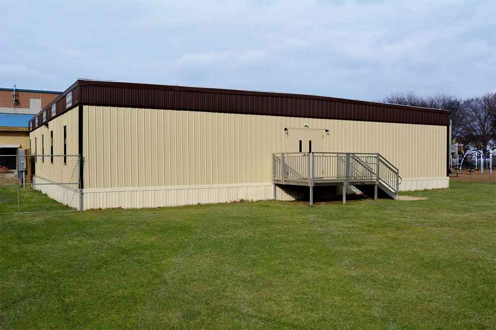 Modular building placed on a paved surface with metal ramp access, surrounded by autumn trees in USA